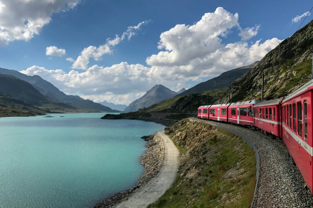 Trem vermelho à beira de um lago de água turquesa nos Alpes suíços